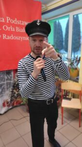 Śpiewak w stroju marynarza pokazuje palcem w kierunku fotografa.