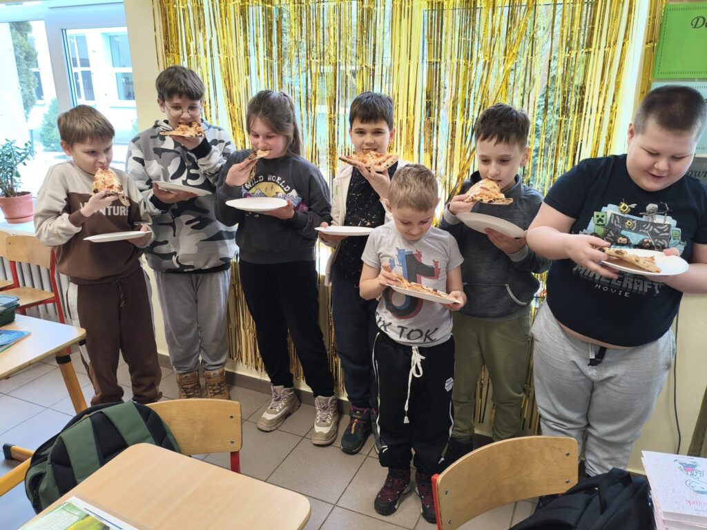 Radosna grupa dzieci trzymająca talerze z pizzą, cieszy się wspólnym jedzeniem i zabawą.