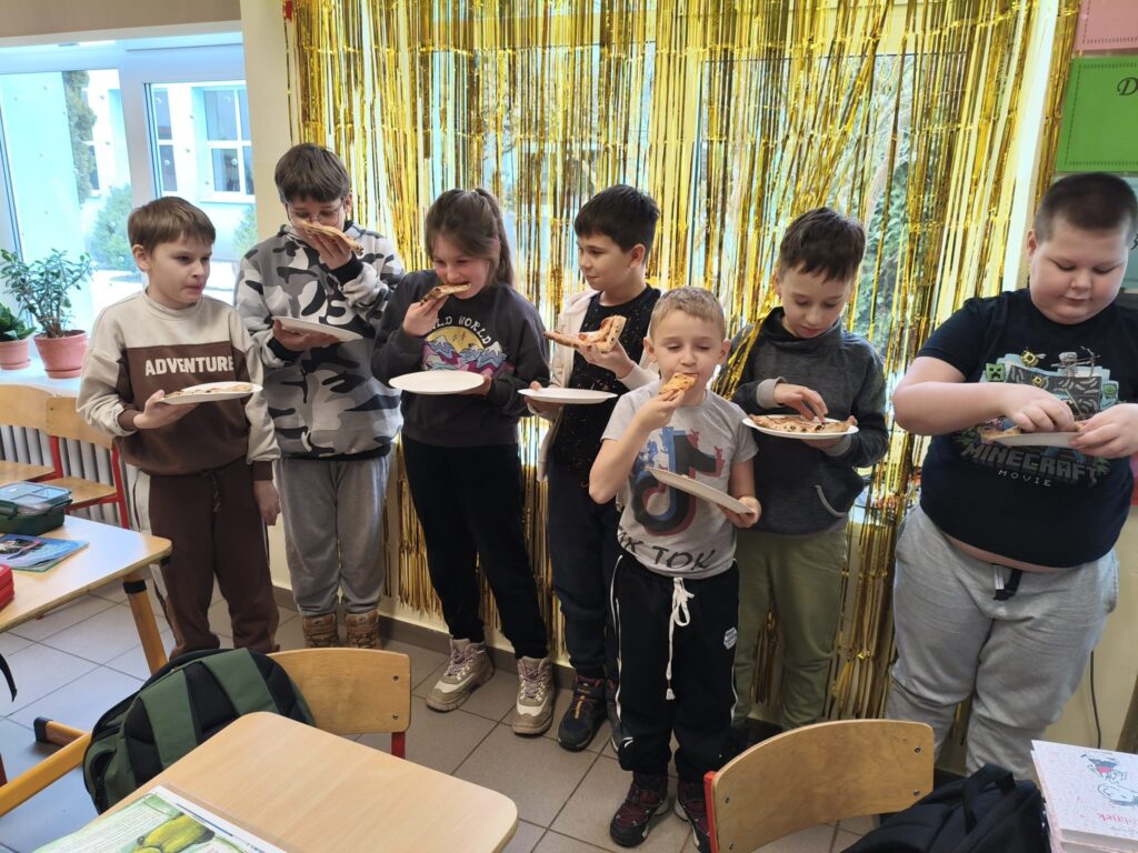 Grupa dzieci trzymająca talerze z pizzą, uśmiechnięta i radosna, cieszy się wspólnym posiłkiem.