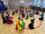 Dzieci w kostiumach siedzą na podłodze sali gimnastycznej