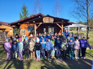Grupa dzieci z opiekunami przed drewnianym budynkiem Zagrody Puchaczówka.