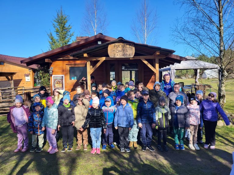 Grupa dzieci z opiekunami przed drewnianym budynkiem Zagrody Puchaczówka.