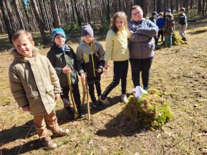 Grupa dzieci podczas leśnej wycieczki z kijkami w rękach.