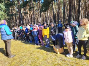 Dzieci ustawione w kolejce w lesie podczas zajęć z przewodnikiem.