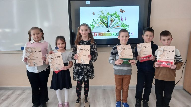 Sześcioro uczniów stoi w klasie przed ekranem z napisem o szkolnym konkursie recytatorskim i prezentuje otrzymane dyplomy oraz nagrody.
