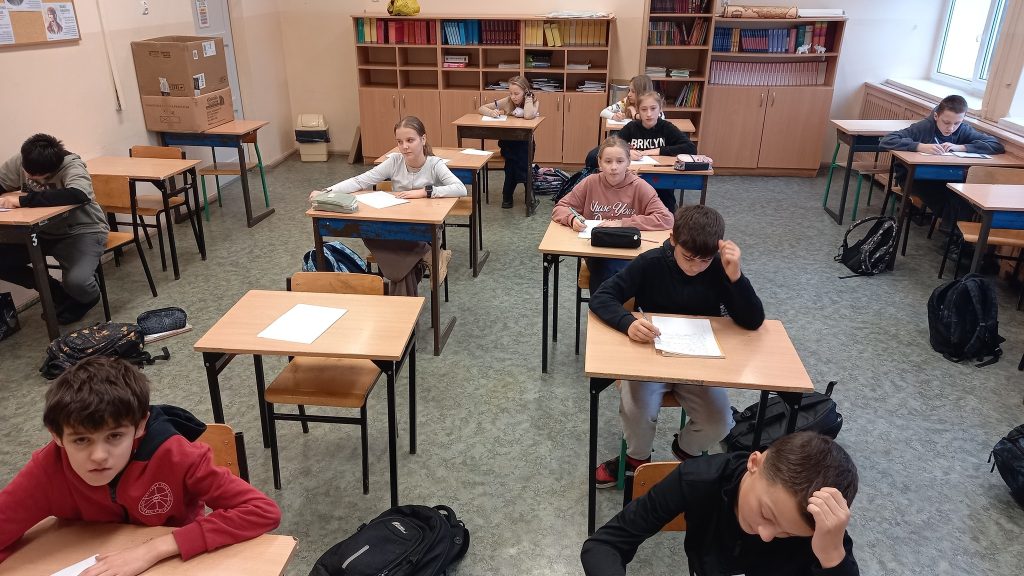 Uczniowie siedzą pojedynczo w ławkach w sali lekcyjnej i piszą pracę podczas szkolnego konkursu.
