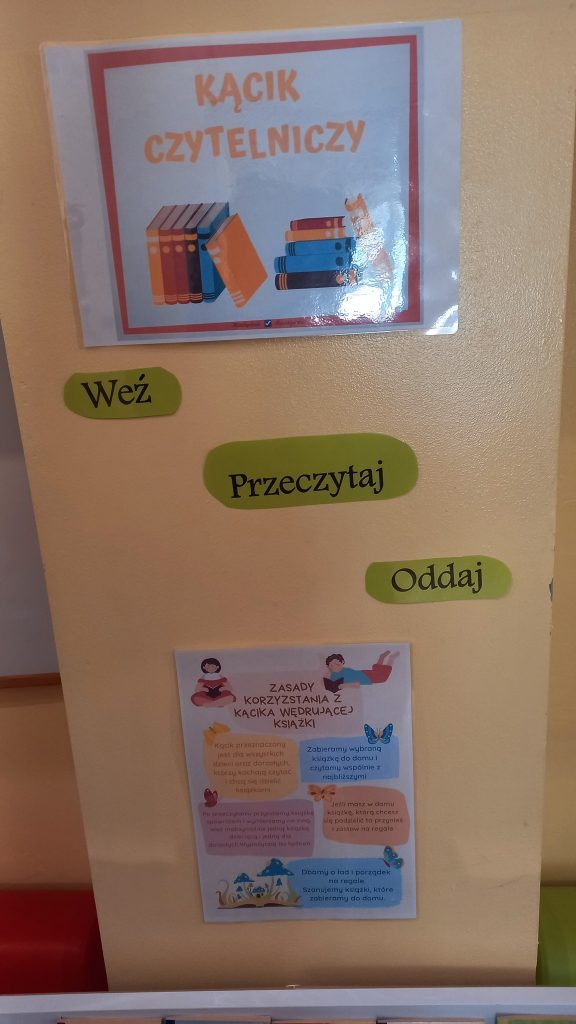 Ściana z napisem ‘Kącik czytelniczy’, hasłami ‘Weź’, ‘Przeczytaj’, ‘Oddaj’ oraz plakatem z zasadami.