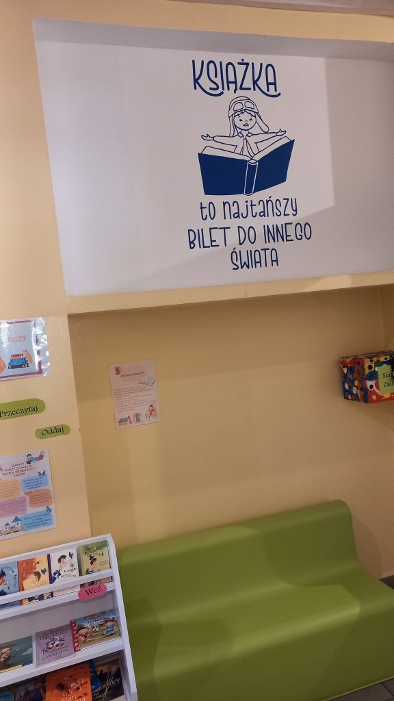 Kącik czytelniczy w bibliotece z napisem „Książka to najtańszy bilet do innego świata