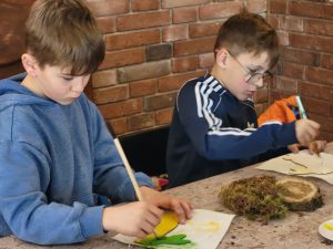 Dwóch chłopców skupionych na malowaniu figurek podczas zajęć plastycznych.