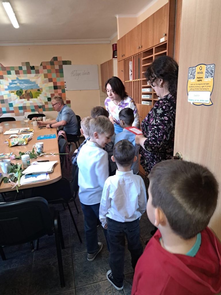Chłopcy wręczają kartki z życzeniami dwóm nauczycielkom w szkolnym pokoju nauczycielskim.