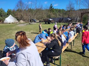Dzieci siedzące przy drewnianych stołach na trawie podczas posiłku na świeżym powietrzu