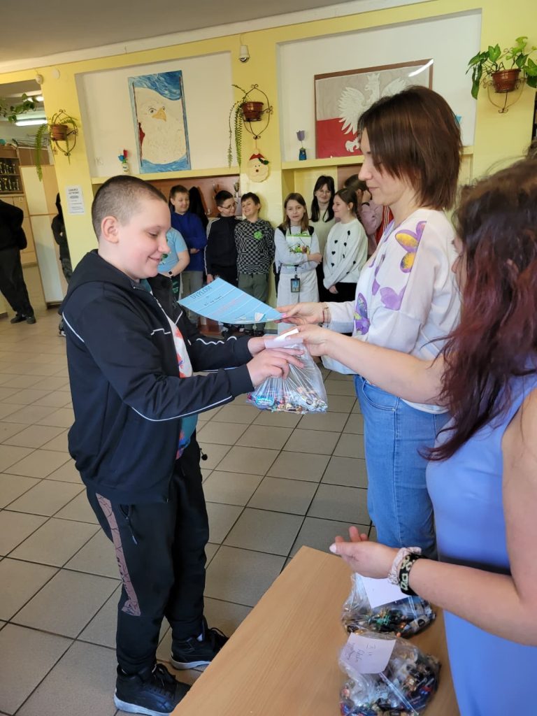 Uczeń odbiera dyplom i upominek podczas wręczania nagród w szkolnym konkursie.