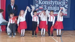 Dzieci w odświętnych biało-czerwonych strojach wykonują układ taneczny, trzymając lekkie chusty w dłoniach.
