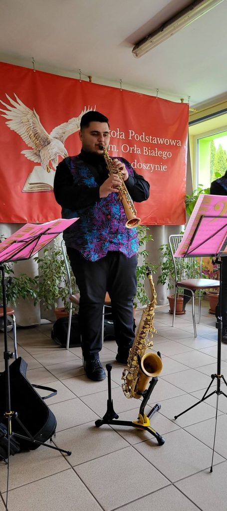 Muzyk grający na instrumencie dętym prezentuje utwór podczas koncertu edukacyjnego dla uczniów szkoły.