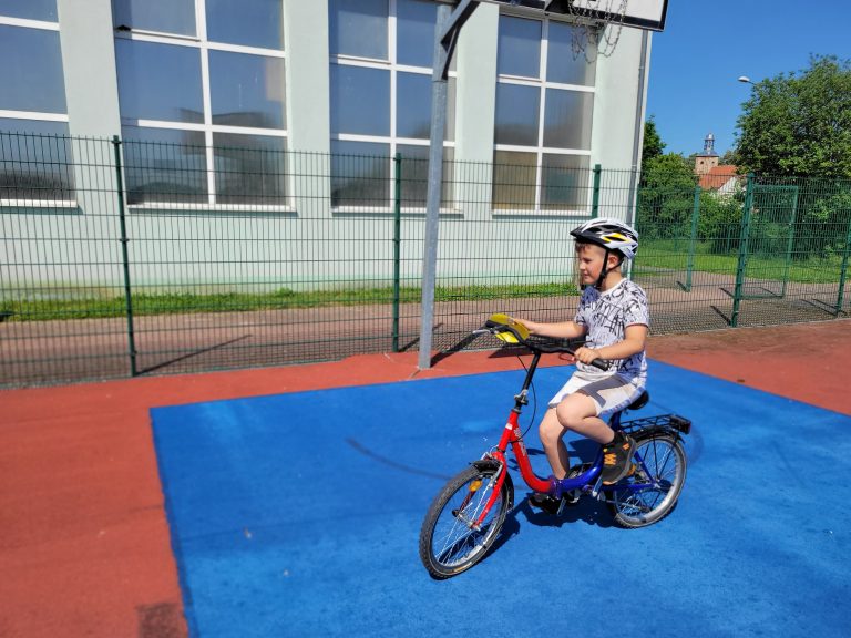 Dwóch chłopców uczestniczy w ćwiczeniach rowerowych na szkolnym boisku sportowym.