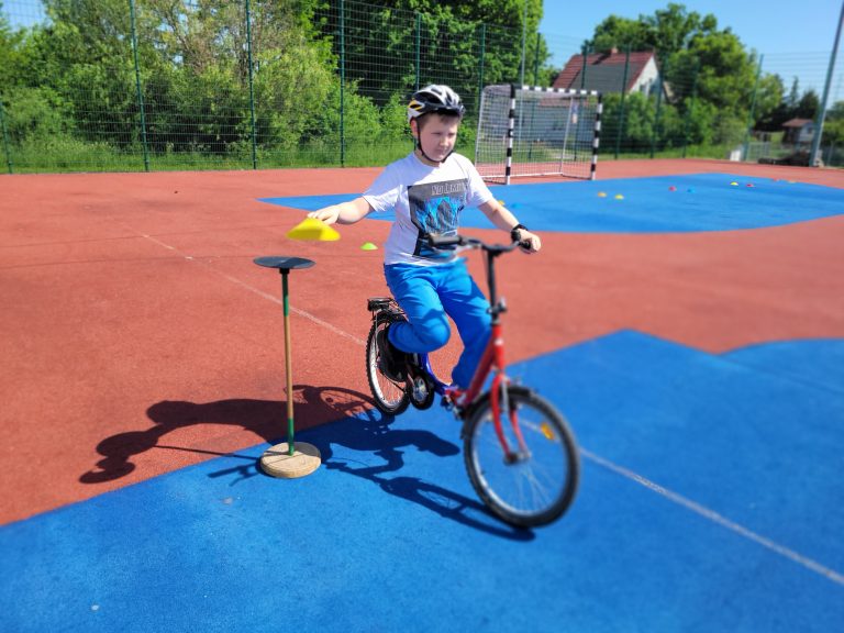 Chłopiec na rowerze przejeżdża obok stojaka z chorągiewką podczas zajęć sportowych.