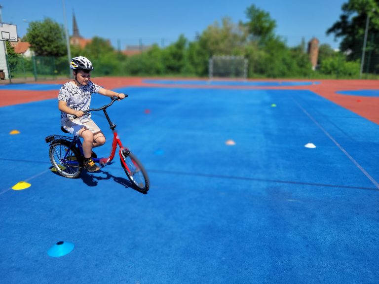 Chłopiec na małym rowerze przejeżdża obok budynku szkoły podczas zajęć sportowych.