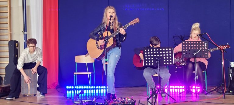 Młodzi muzycy wykonują utwór na gitarach i cajonie podczas szkolnego koncertu profilaktycznego.