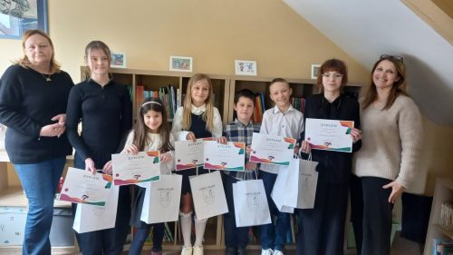 Uczniowie z nauczycielami prezentują dyplomy i nagrody po szkolnym konkursie w bibliotece.